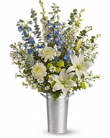 Tall arrangement of white lilies, mums, and blue delphinium in a silver metal bucket.