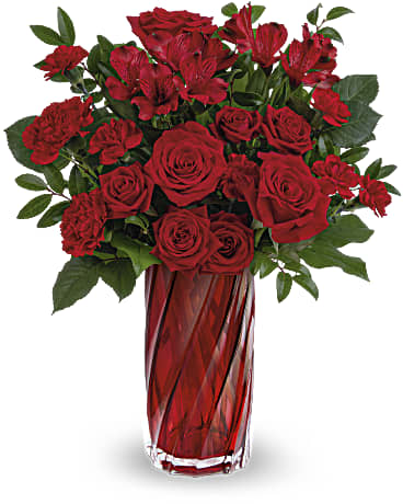Tall arrangement of red roses, carnations, and alstroemeria in a red glass vase