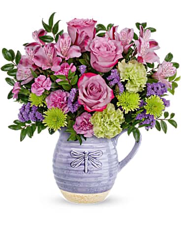 Mixed pink, green, and purple flower arrangement in a lavender ceramic pitcher with dragonfly motif