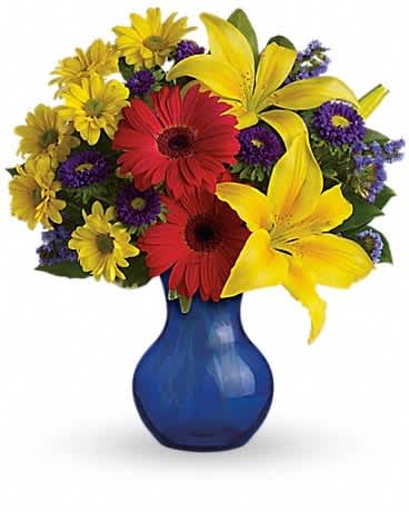 Bright bouquet of yellow lilies, red gerbera daisies, and mixed blooms in a blue glass vase