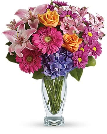 Bright mixed bouquet of pink lilies, gerberas, orange roses and purple blooms in a clear glass vase