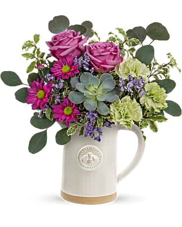 Mixed bouquet of pink roses, magenta daisies, green carnations, and a succulent in a white ceramic pitcher