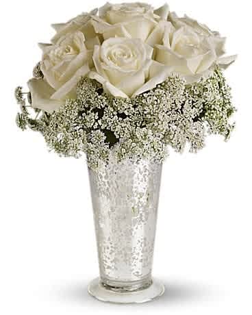 Tall silver glass vase with white roses and tiny white filler flowers arranged in a dome.