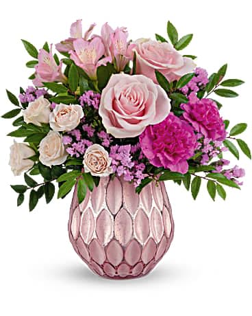 Pink and cream roses, carnations, and mixed blooms arranged in a pink textured glass vase