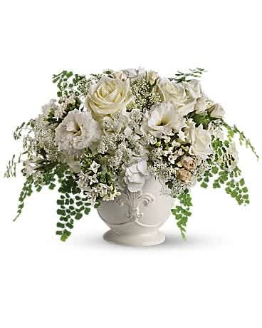 Low white urn of white roses and blooms with trailing ferns in a full rounded arrangement