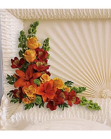 Corner casket spray with orange lilies, yellow roses and red flowers inside a cream casket.