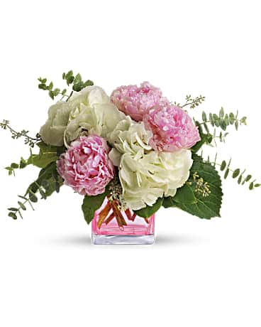 Low arrangement of pink peonies and white hydrangeas in a clear cube vase with pink water
