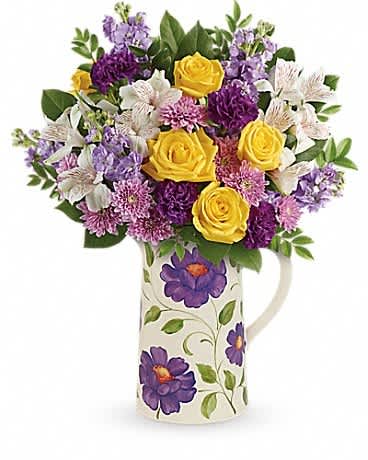 Yellow roses and purple flowers in a patterned ceramic pitcher with painted purple blooms