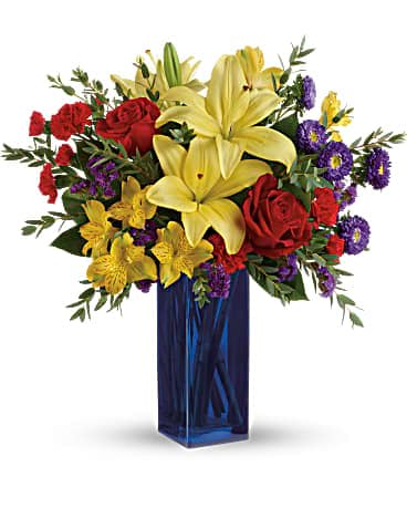 Tall arrangement of yellow lilies, red roses, and purple asters in a blue glass vase