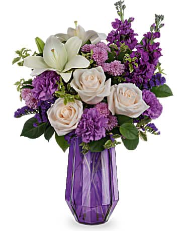 Purple and white mixed flower arrangement with lilies and roses in a tall faceted purple glass vase