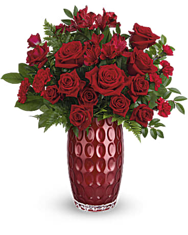 Arrangement of red roses and accent blooms in a tall red textured glass vase