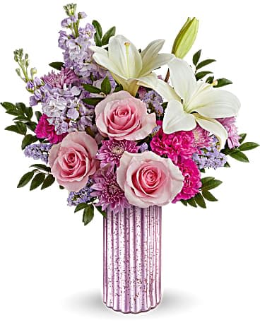 Pink and white bouquet with roses, lilies, and mixed flowers in a tall pink glass vase