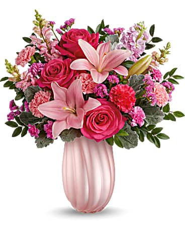 Pink lilies, roses, and carnations arranged in a fluted light pink vase