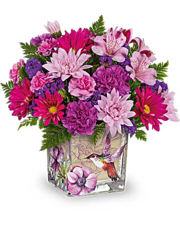 Bright pink and purple mixed flower arrangement in a square glass vase with a hummingbird illustration