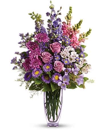 Tall arrangement of purple asters, pink roses, and mixed blooms in a clear glass vase