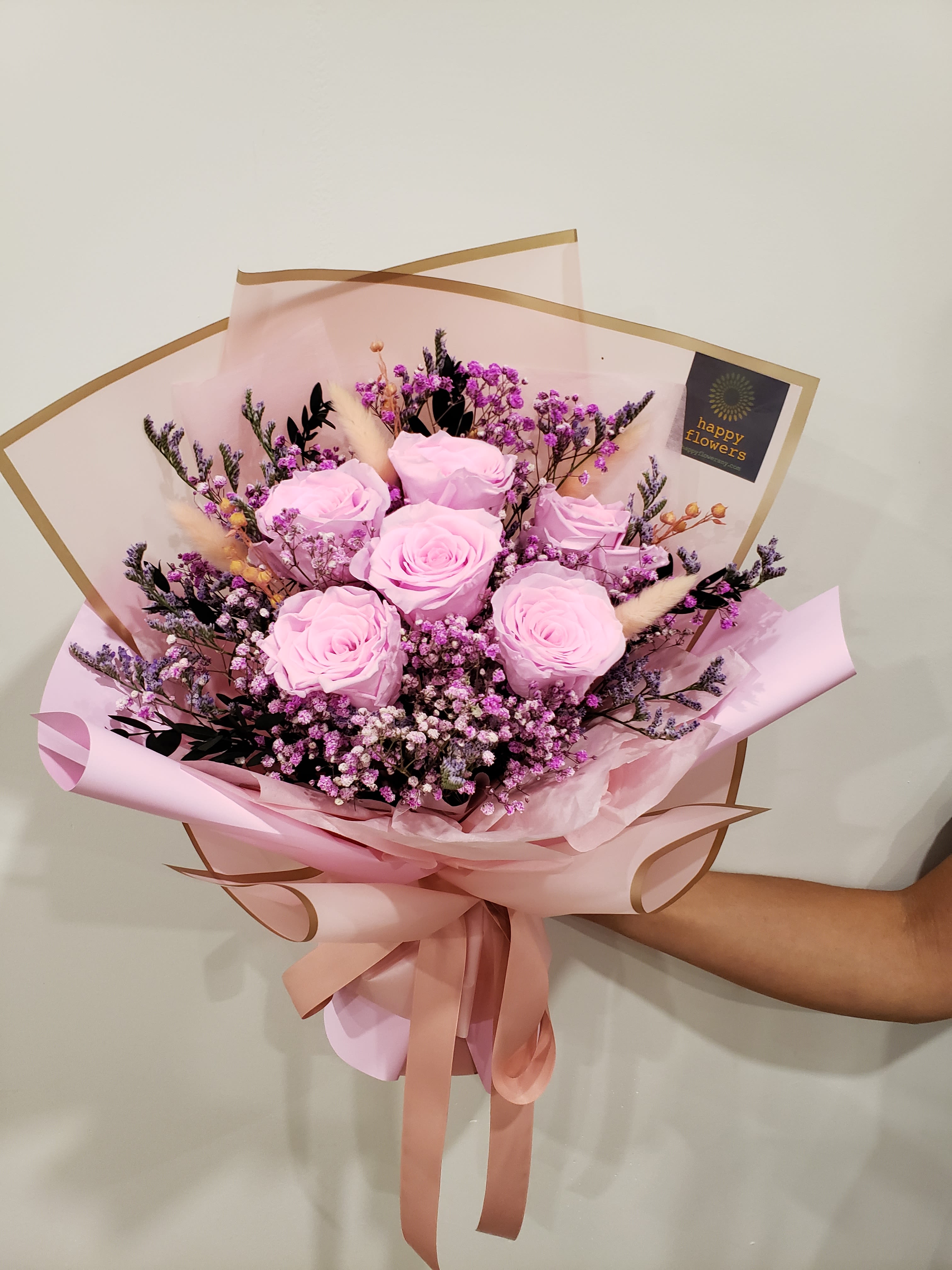 Bouquet of pale pink roses with purple filler flowers wrapped in pink paper