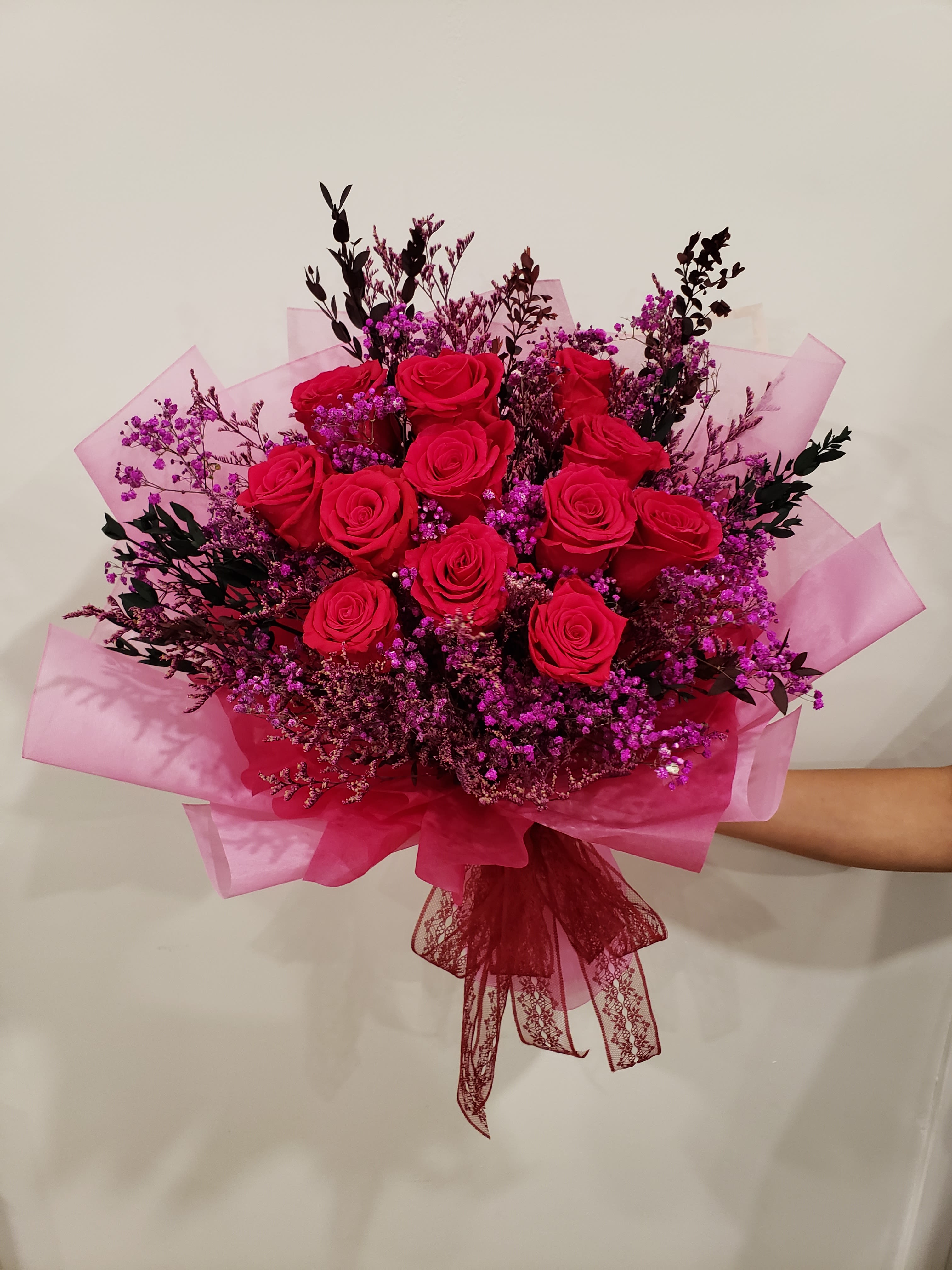Bouquet of red roses with purple filler flowers wrapped in pink paper