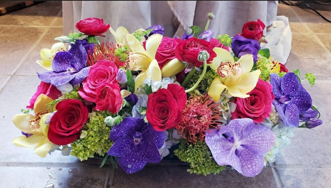 Colorful bouquet of roses, orchids, and lilies arranged low and wide