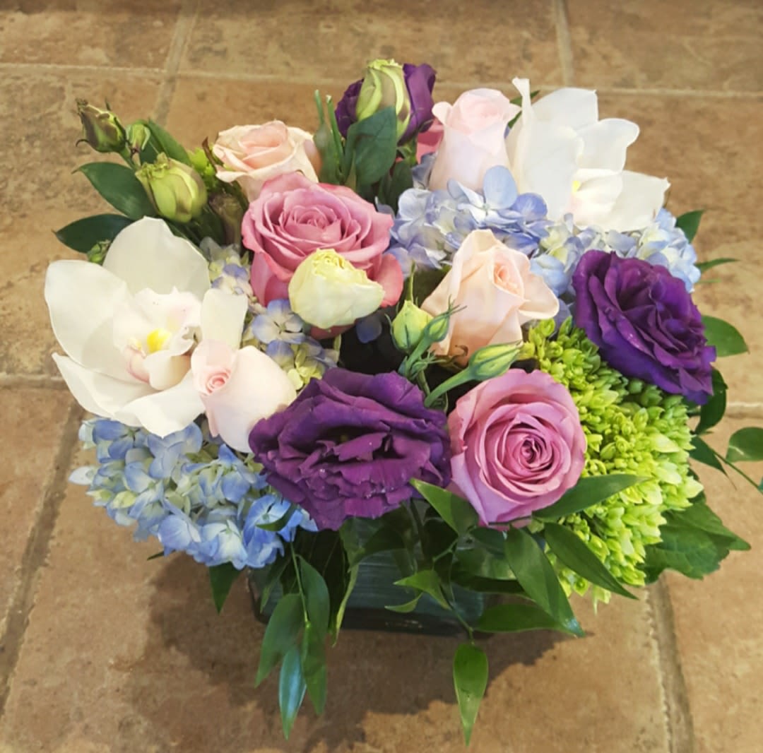 Mixed bouquet of roses, orchids, and hydrangeas in a low container