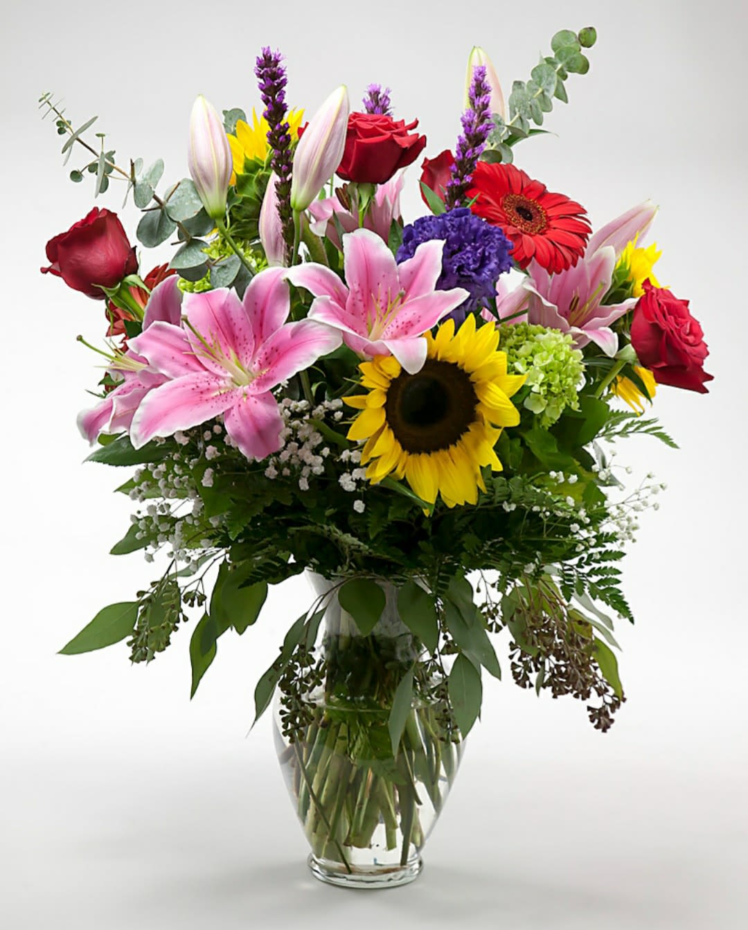 Mixed bouquet of lilies, roses, and sunflowers in a glass vase