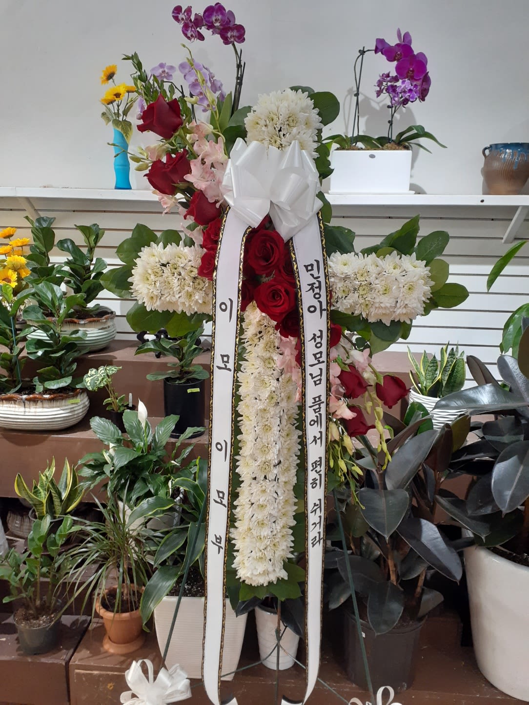 Tall standing floral wreath with red roses, white chrysanthemums, and orchids