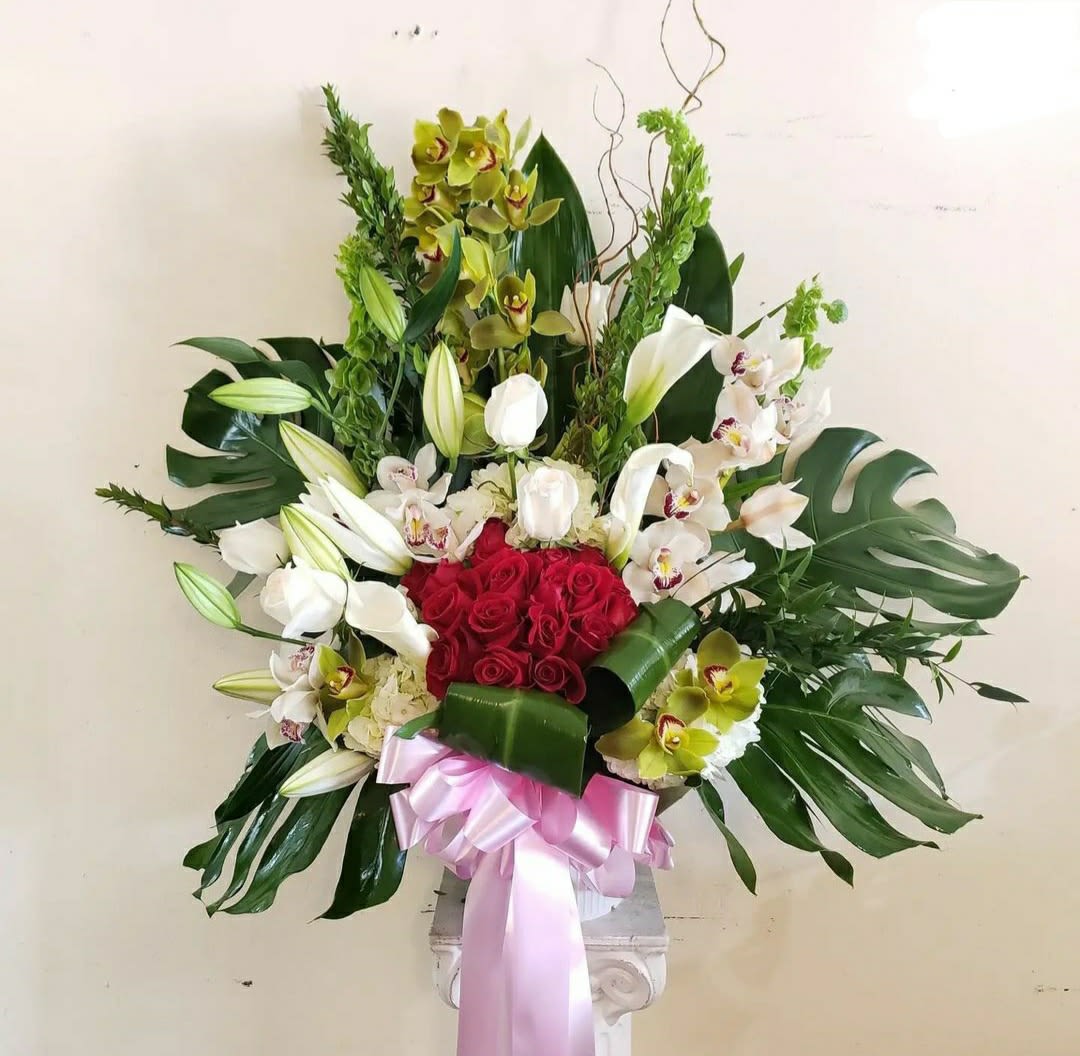 Large floral arrangement with red roses, white orchids, and lilies in a pedestal vase