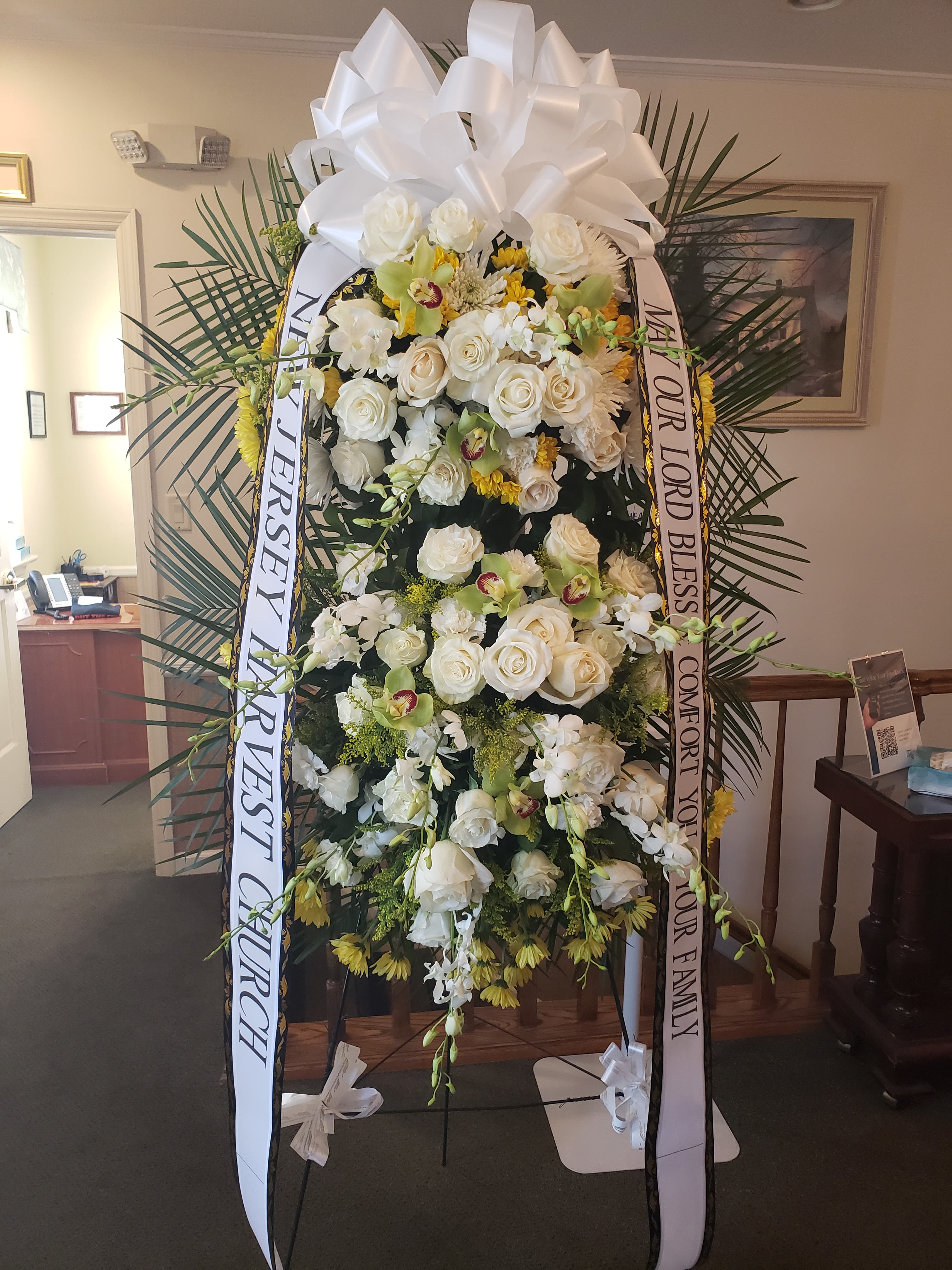 Large white funeral spray with roses and ribbons on a stand