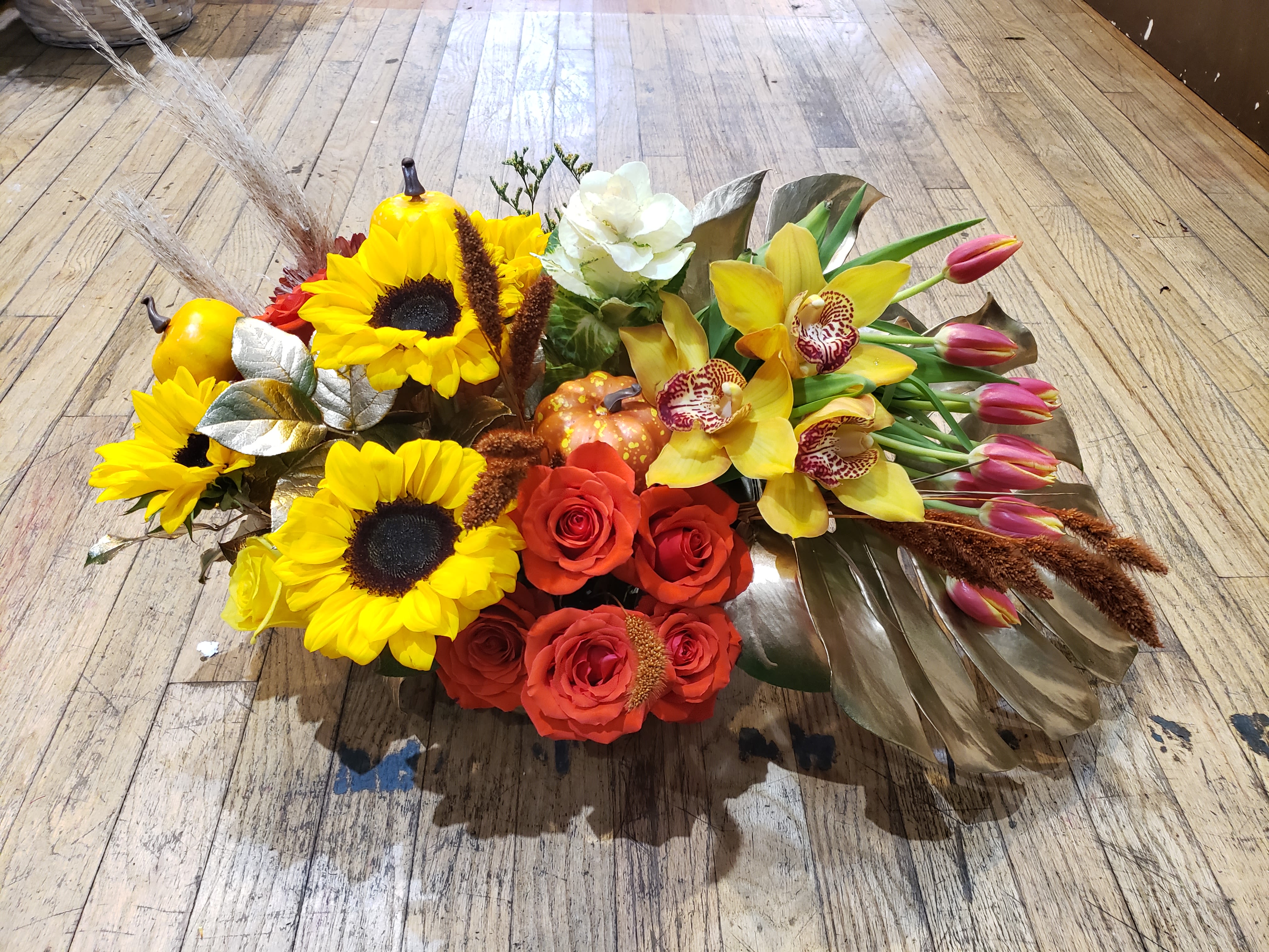 Mixed bouquet with sunflowers, roses, orchids, and tulips on a wooden floor