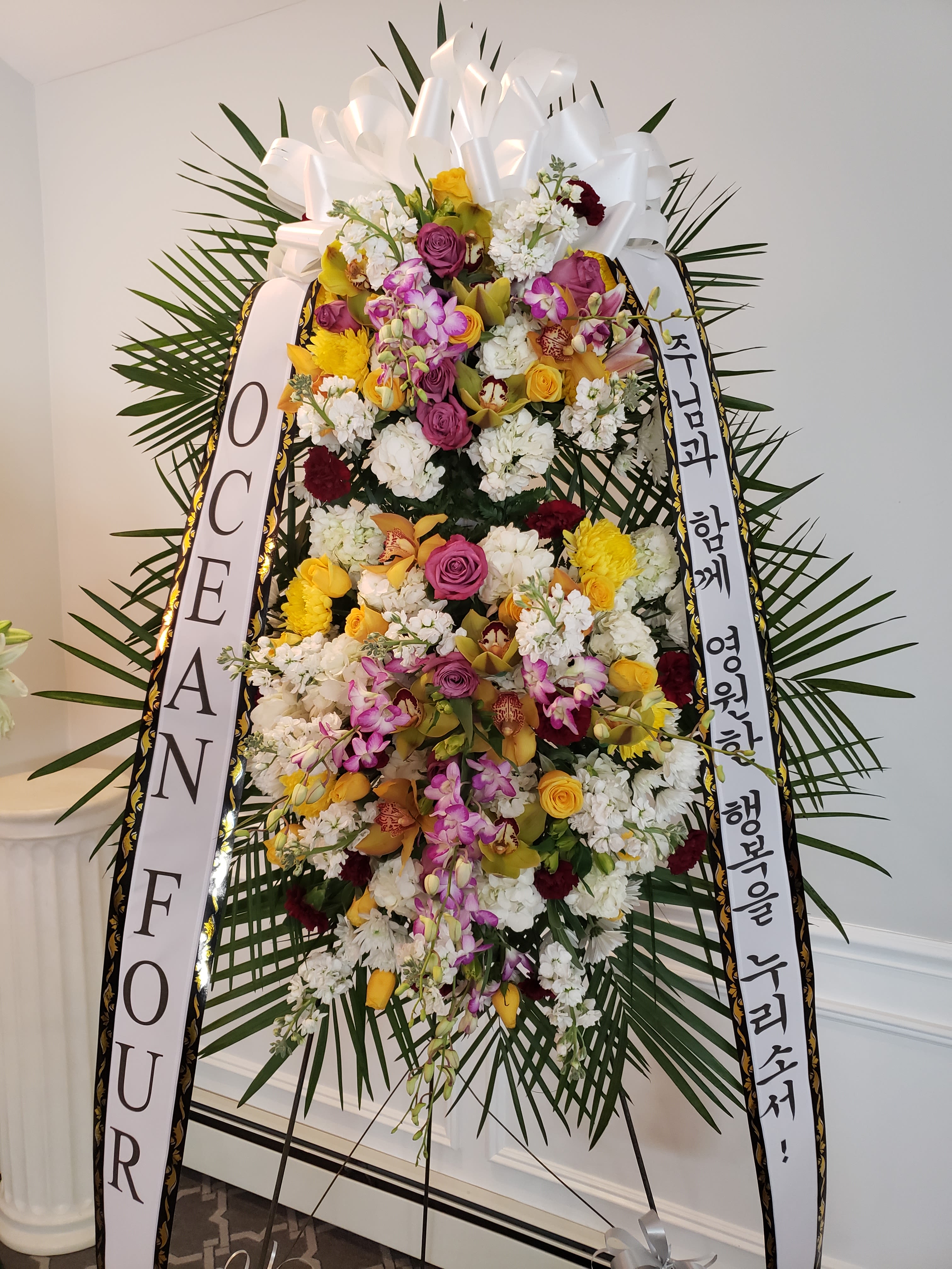 Tall standing floral wreath with white ribbons and mixed blooms