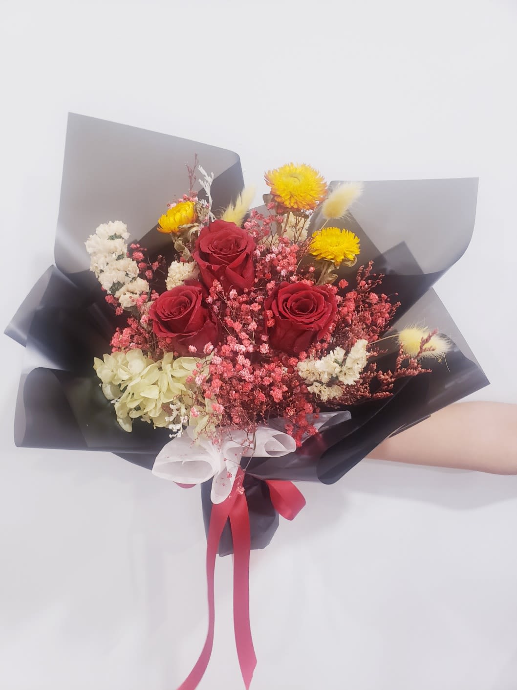 Bouquet of red roses with yellow and white filler flowers wrapped in black paper