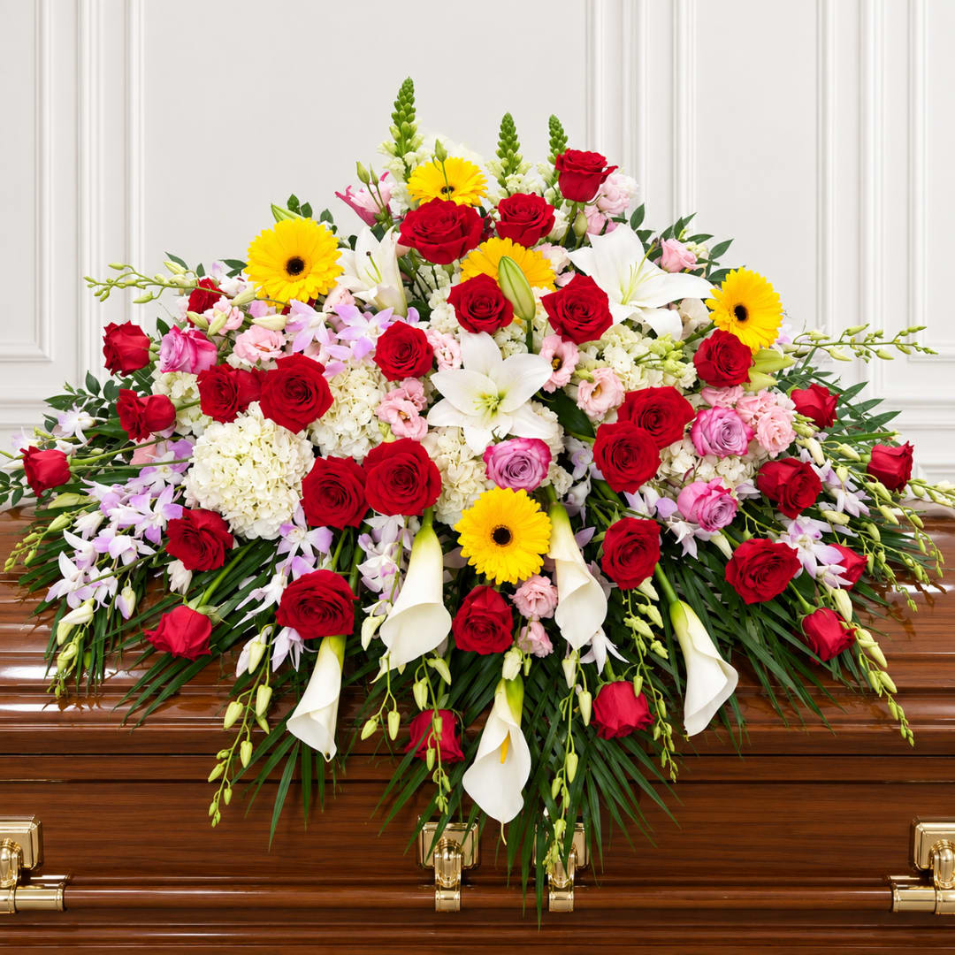 Large floral spray on a casket with red roses, white lilies, and yellow daisies