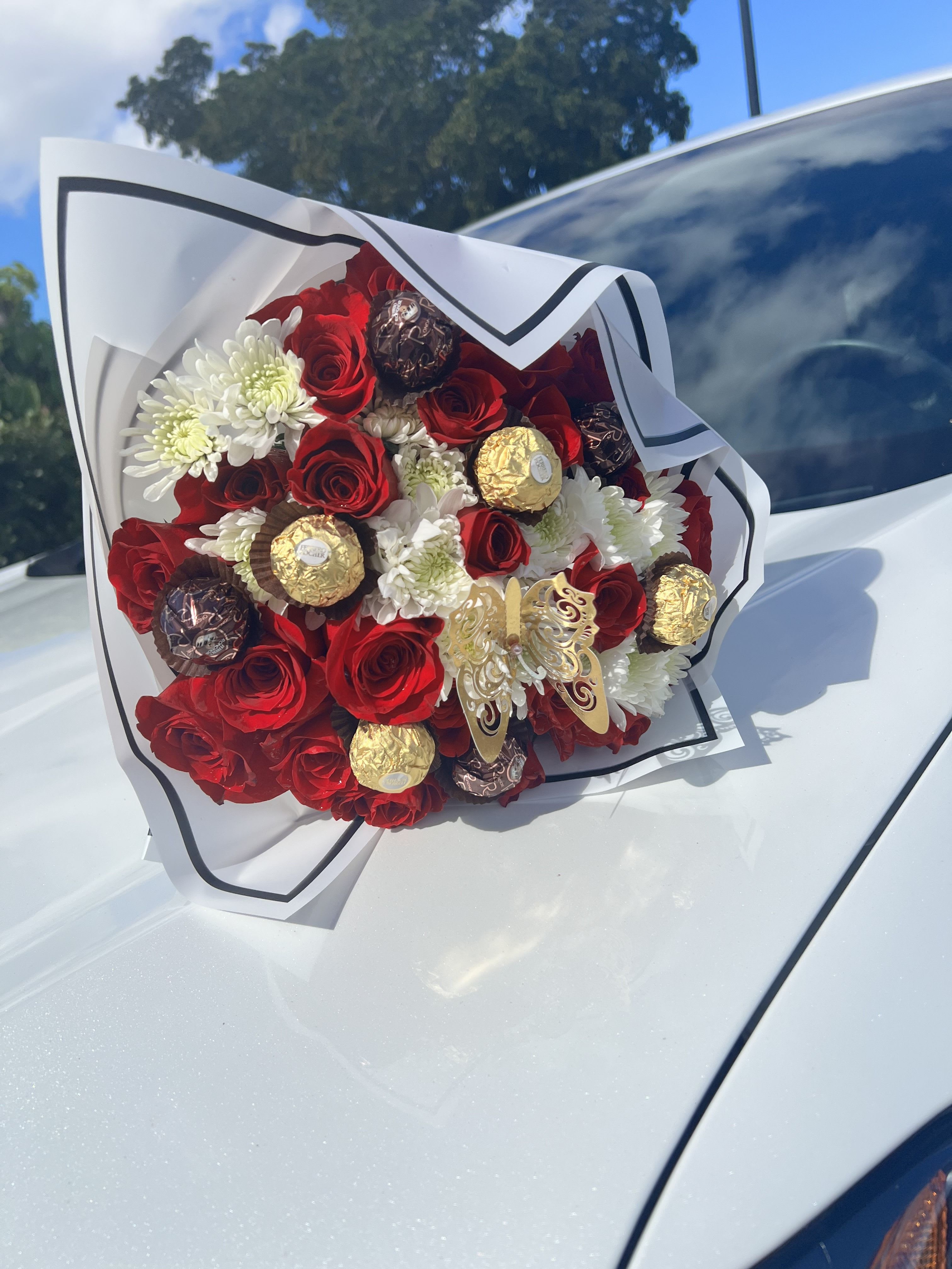 Bouquet of red roses, white daisies, and wrapped chocolates on a car hood