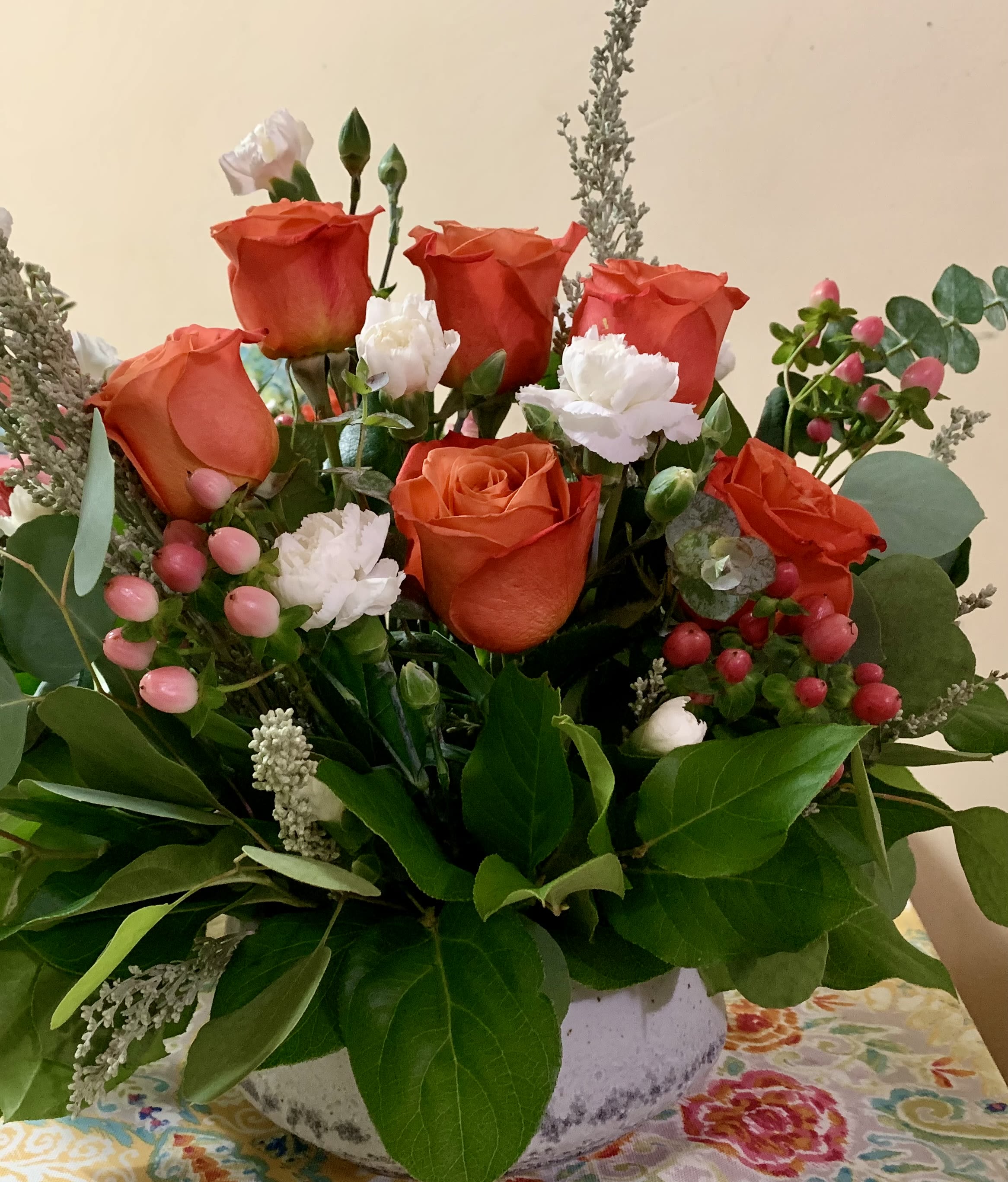 Orange roses and white carnations in a white vase with greenery and pink berries