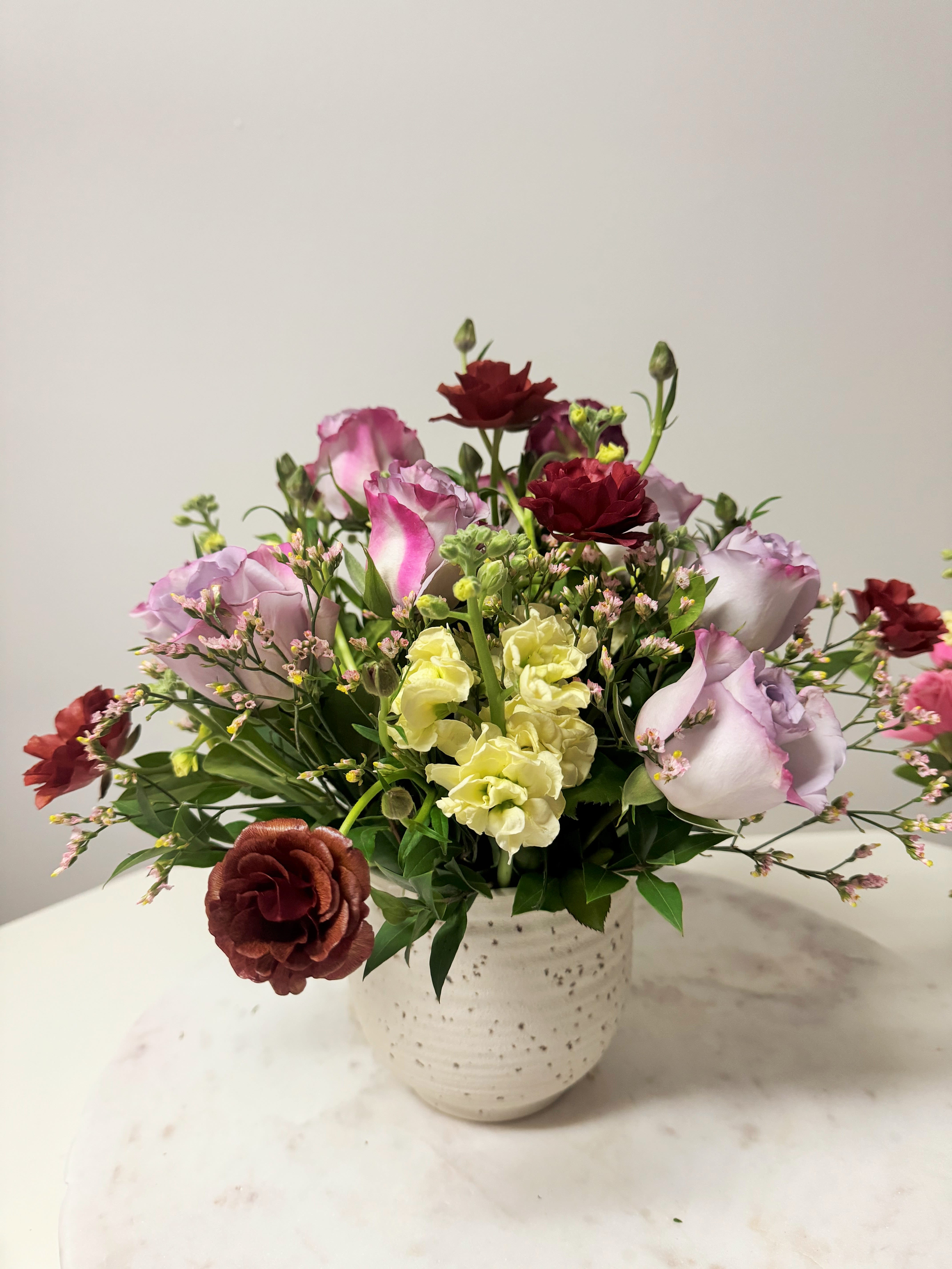 Mixed bouquet of pink, lavender, yellow, and burgundy flowers in a white vase