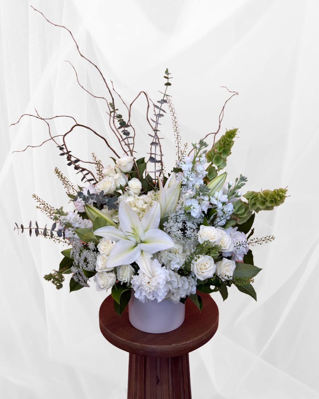 White floral arrangement with lilies and roses in a pale vase