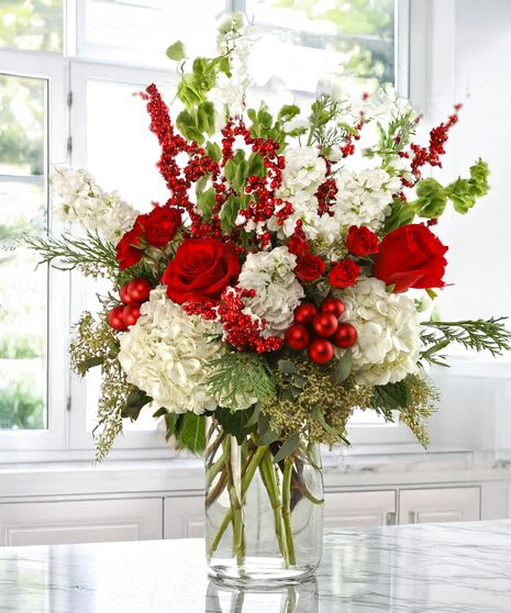 Red roses and white hydrangeas in a clear glass vase with red berry accents