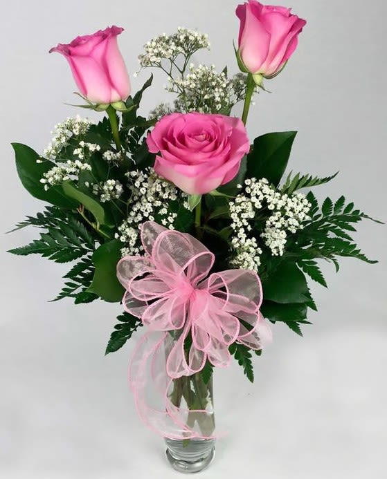 Pink roses in a clear glass vase with baby's breath and a pink ribbon bow