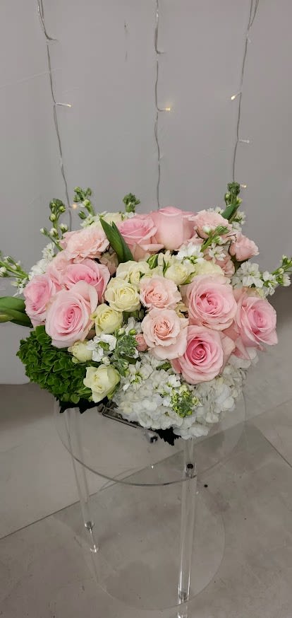 Round arrangement of pink and cream roses with white hydrangeas on a clear stand