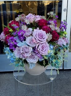 Round arrangement of lavender and red roses with purple blooms in a light ceramic bowl