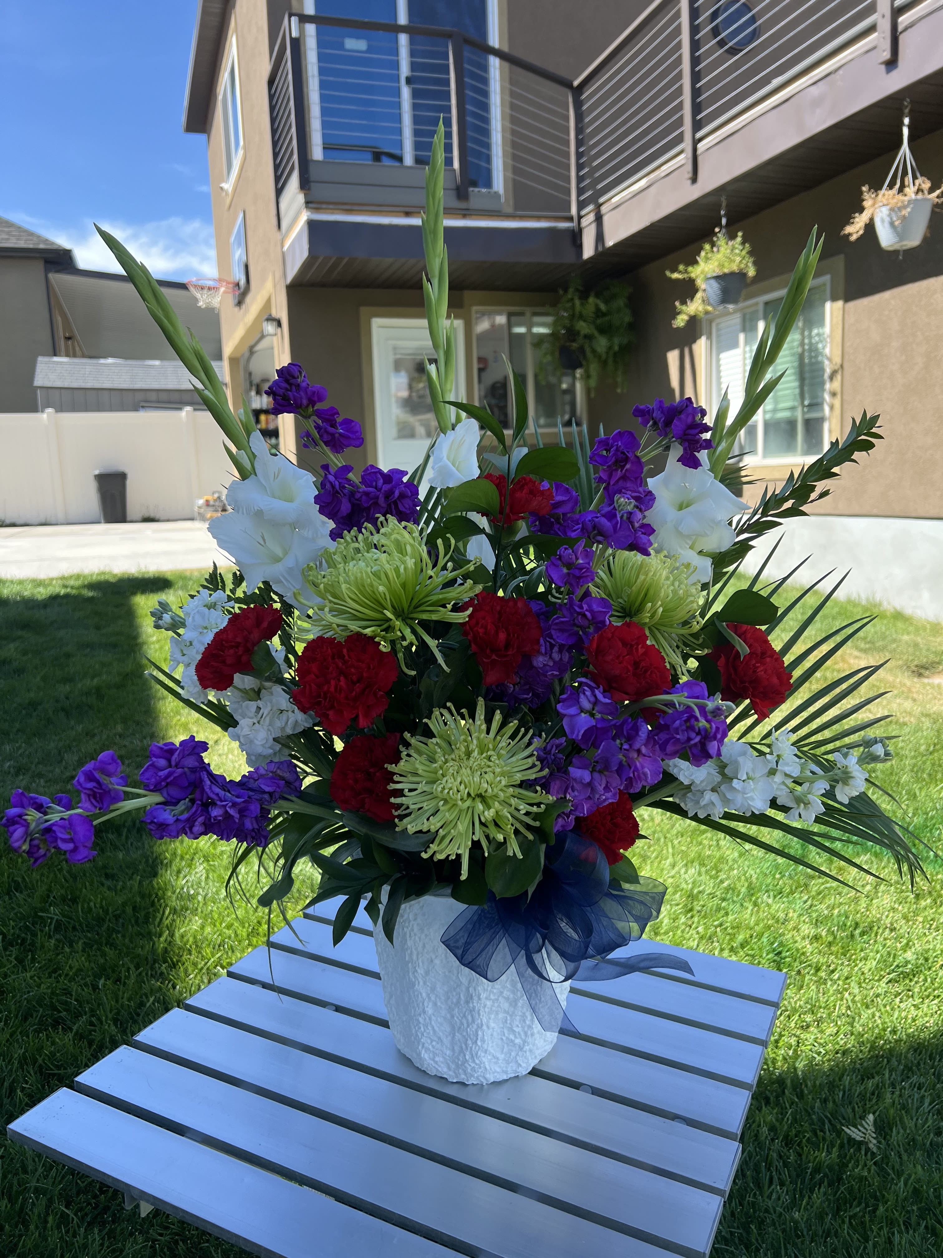 Large mixed floral arrangement in a white vase with purple, red, and white blooms