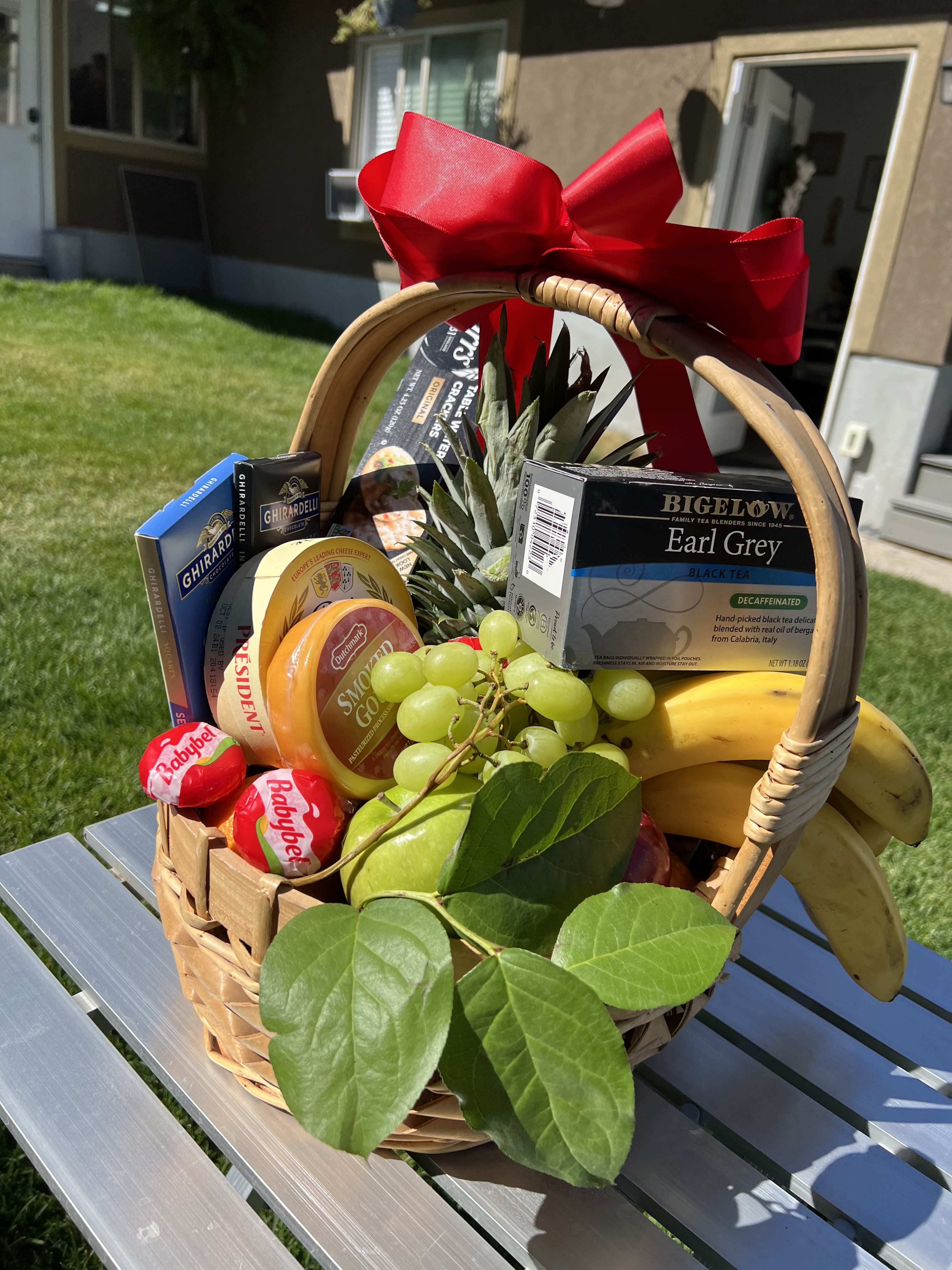 Gift basket with fruit, tea, cheese, and chocolates tied with a red bow