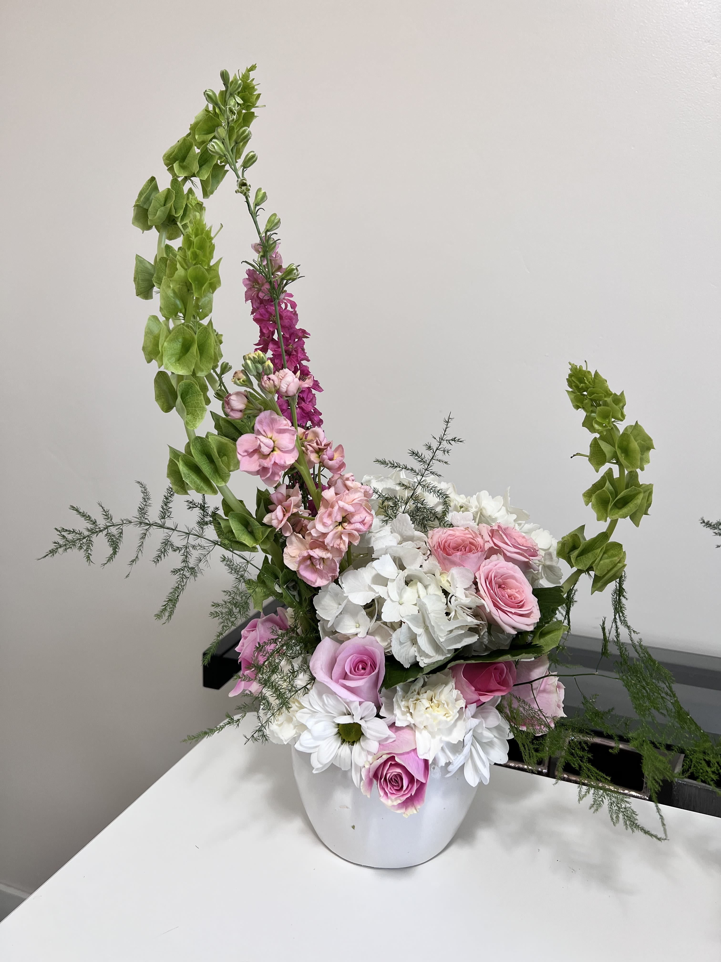 Pink roses and white hydrangeas in a white vase with tall green accents