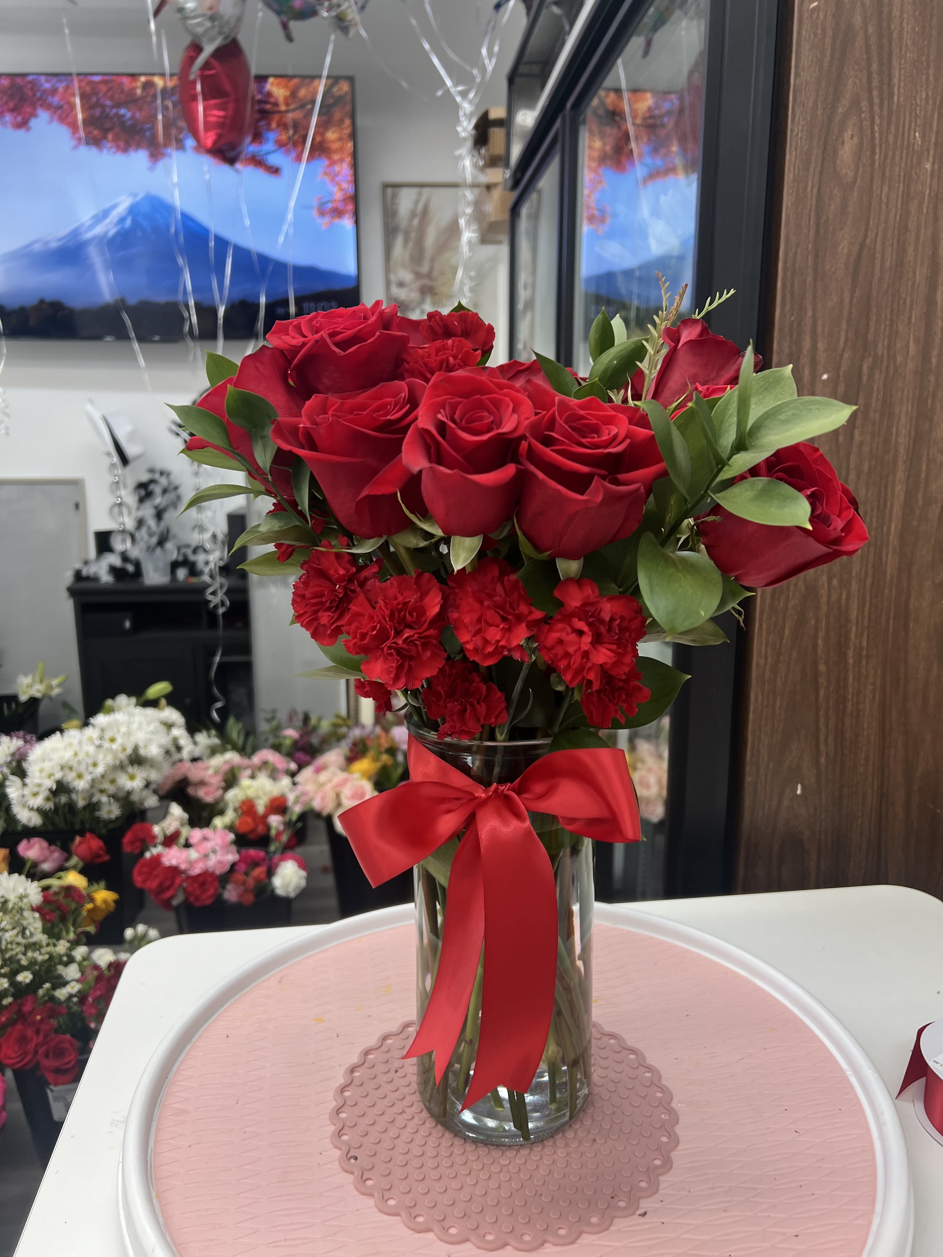 Red roses and carnations in a clear glass vase with a red ribbon.