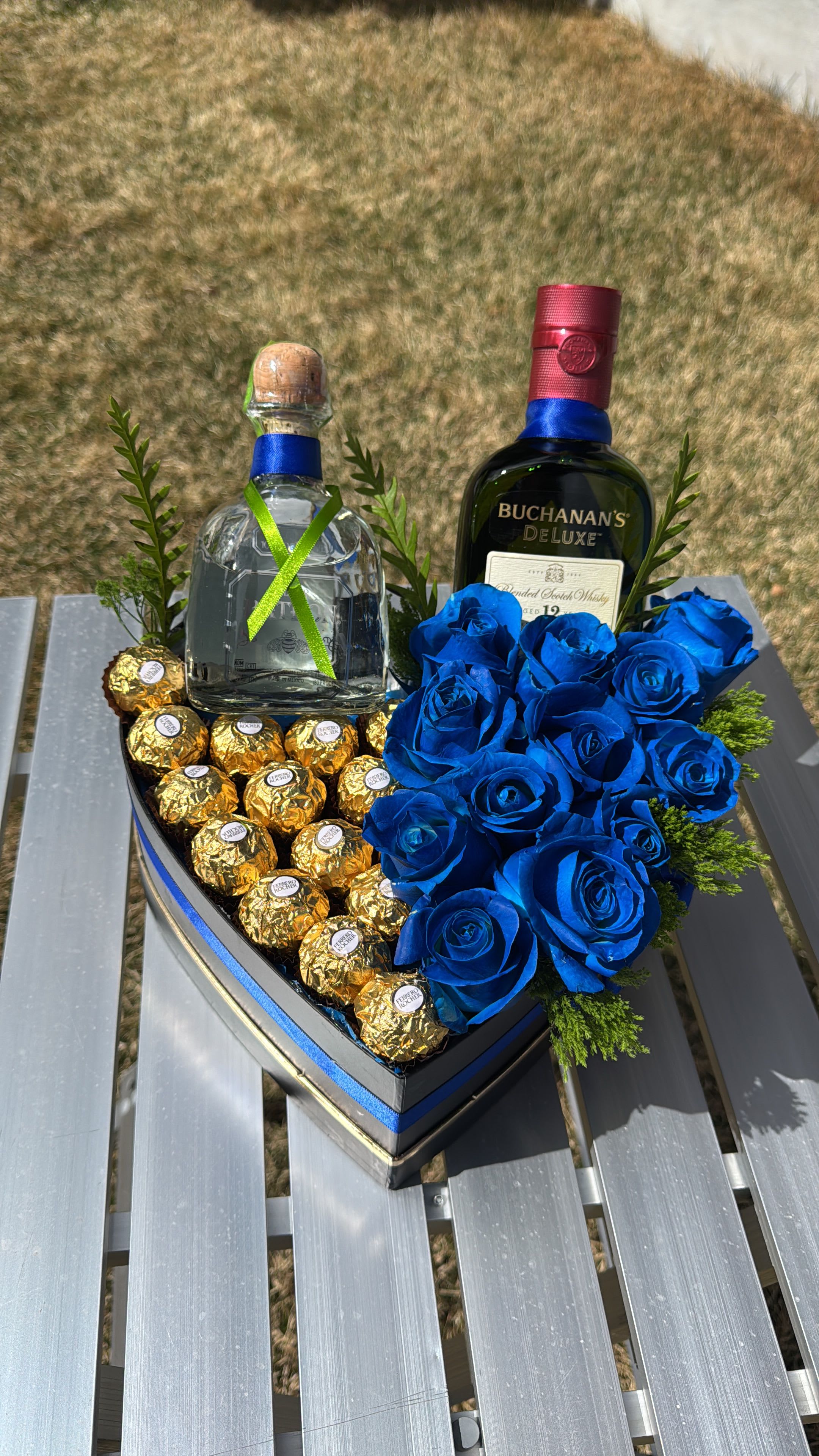 Heart-shaped gift box with blue roses, chocolates, and two liquor bottles