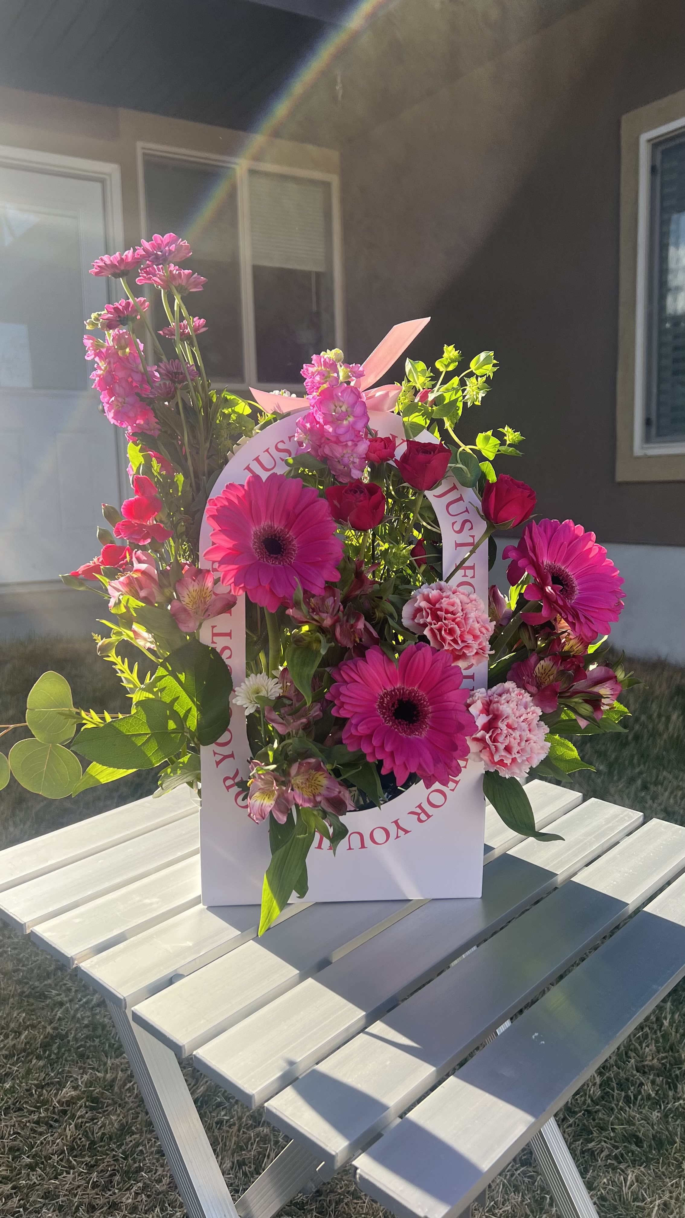 Pink gerbera daisies and roses arranged in a white gift bag