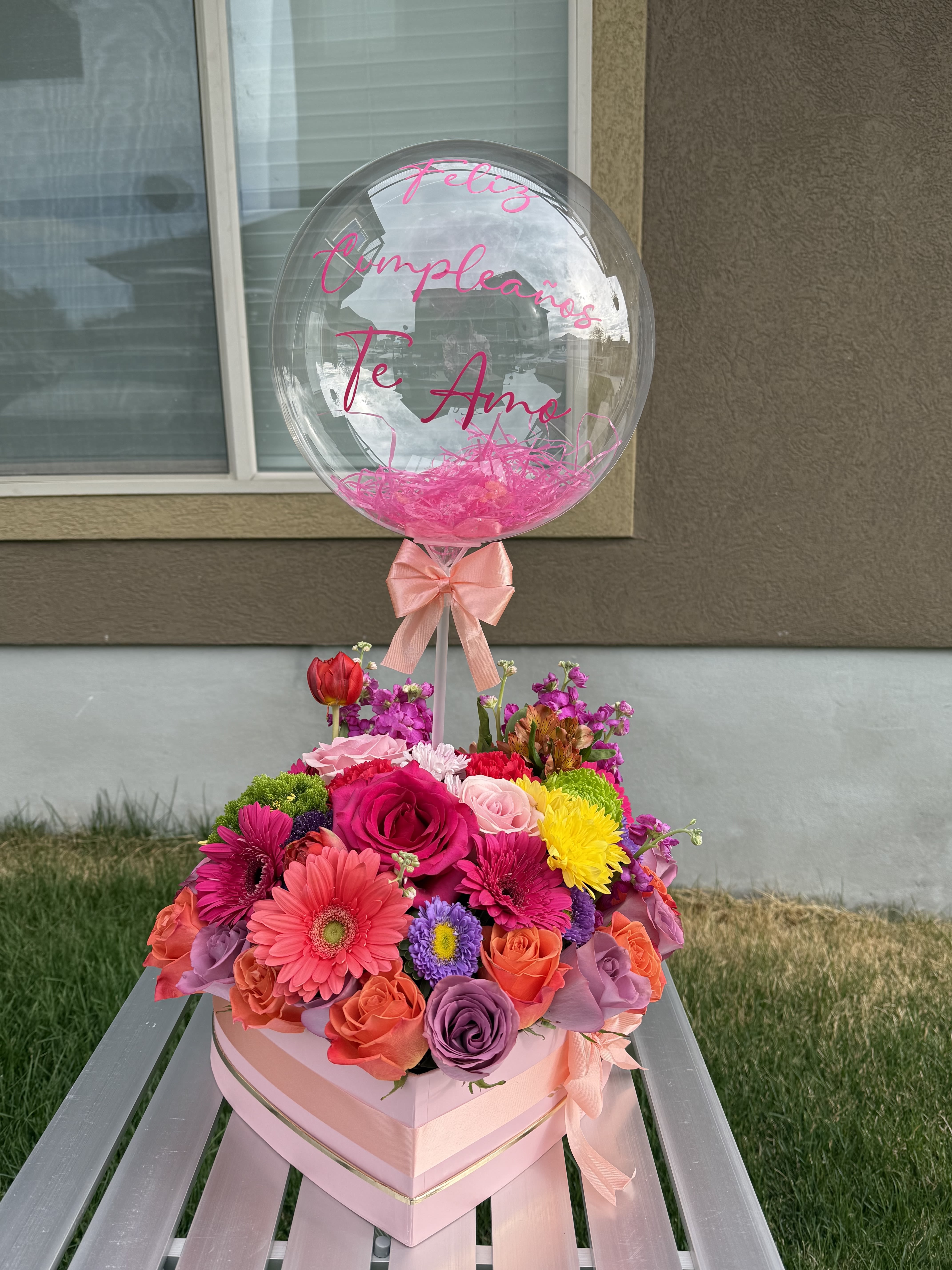 Pink balloon over a colorful flower box with roses and gerbera daisies