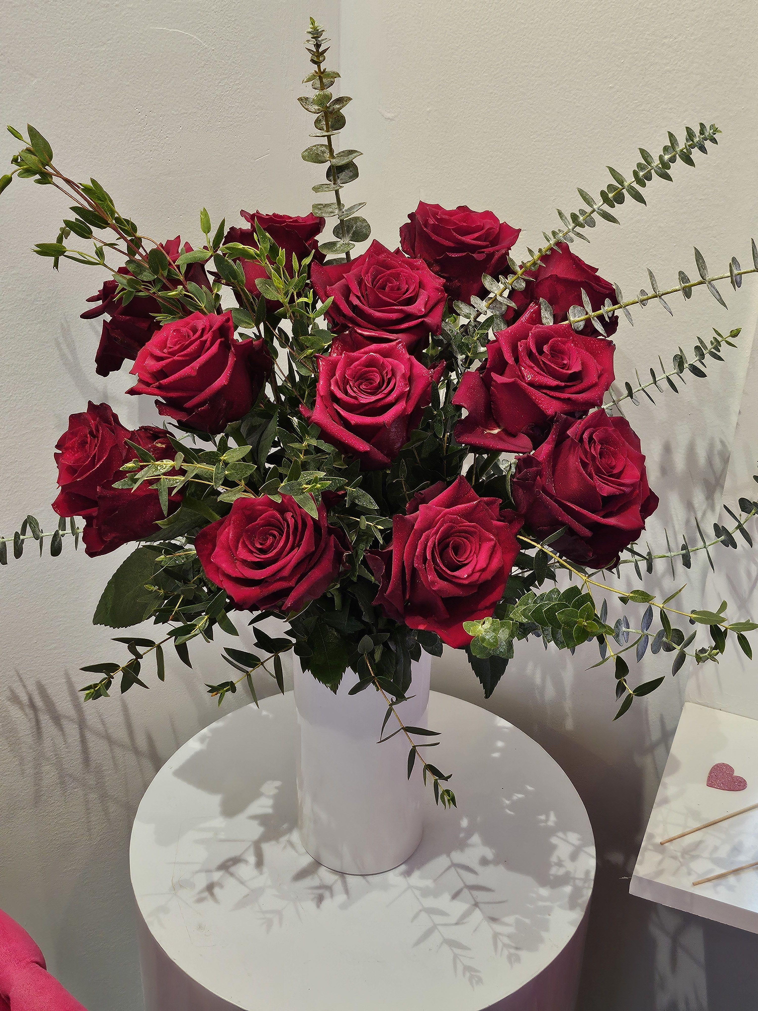 Bouquet of deep red roses in a white vase with airy greenery
