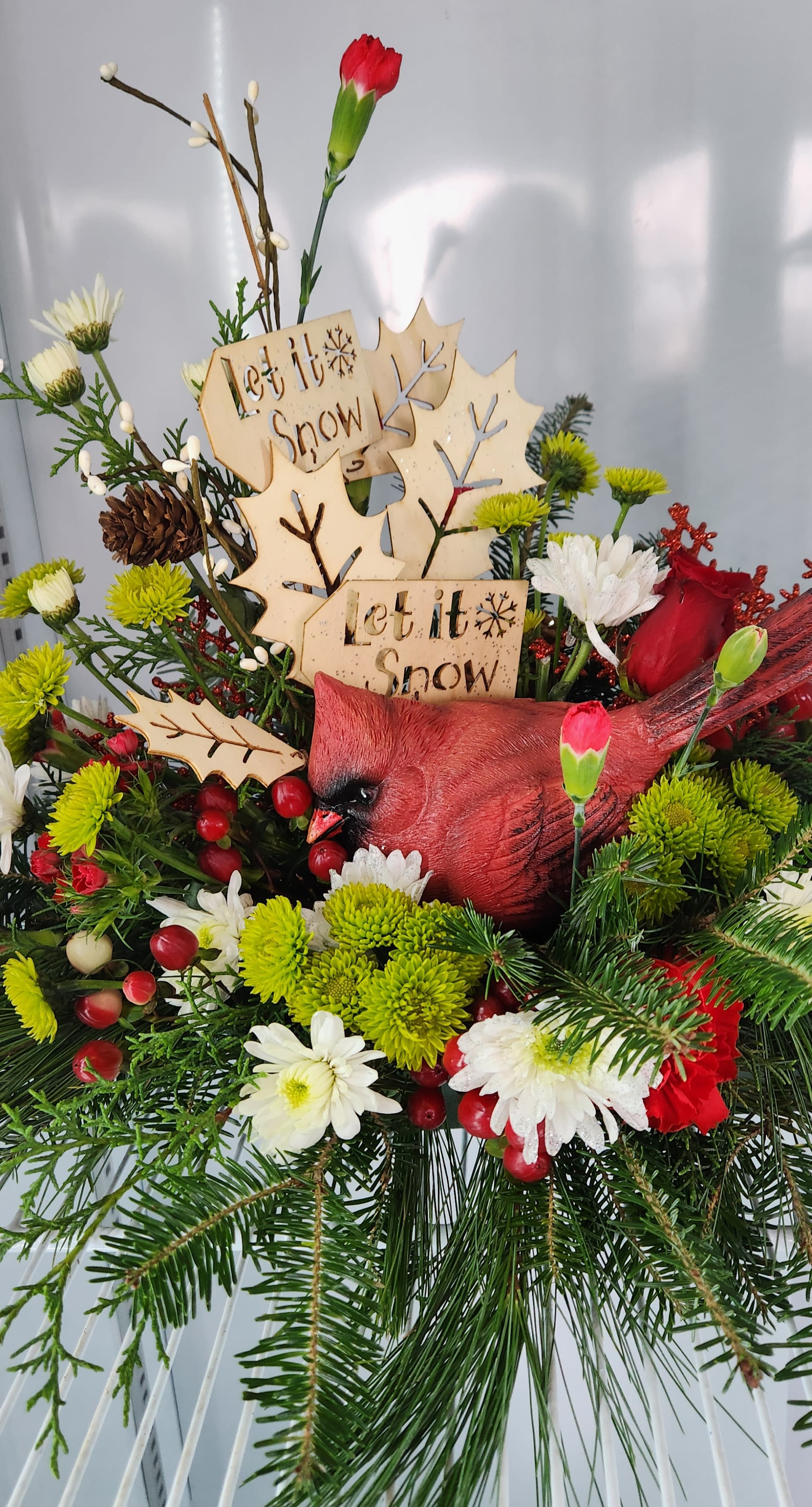 Let it Snow Cardinal  - Keepsake Cardinal, nested in mixed winter evergreen, mini carnations, green ball dianthus, and white mums.