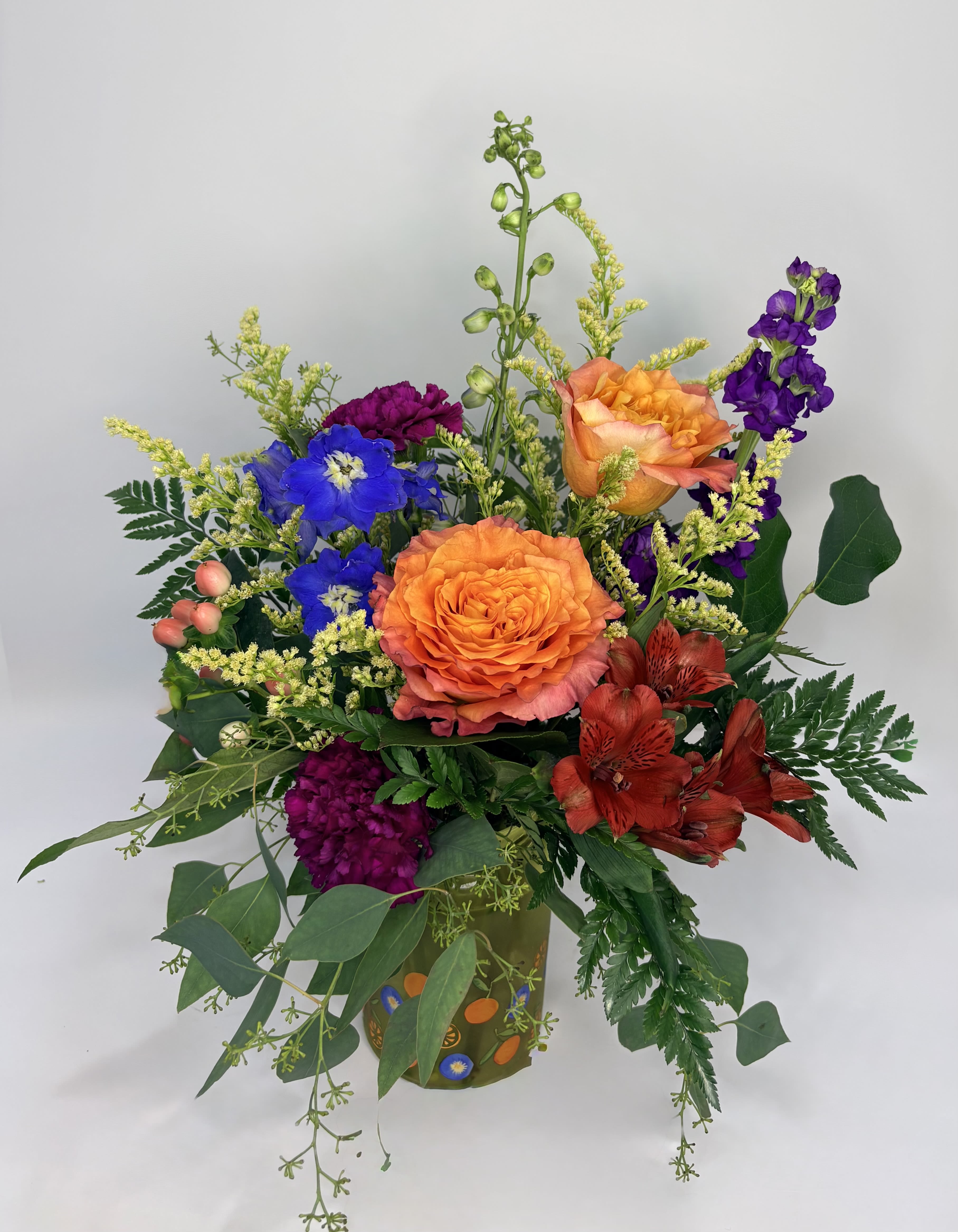 Fruit Punch - Fruit Punch is a delicious mix of orange roses, blue delphinium, purple stock, purple carnations, pink hypericum, and accented with solidago. The vase displays a cute design of oranges and blueberries. Get yourself or a friend some Fruit Punch!
