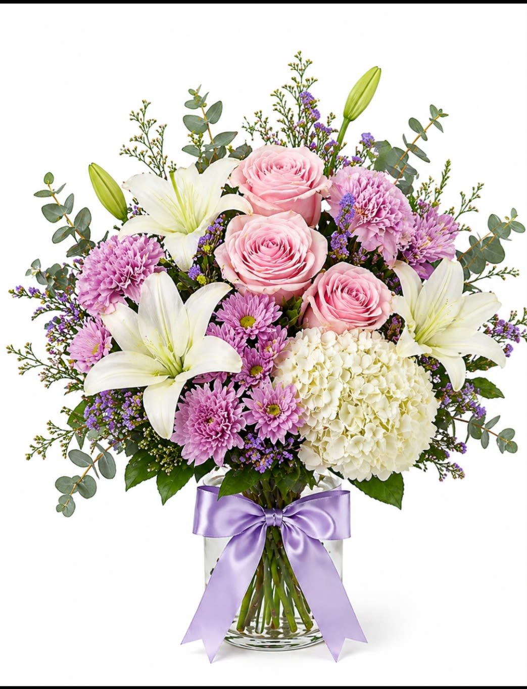 Lavender Grace Bouquet - A soft and elegant arrangement featuring blush pink roses, fragrant white lilies, white hydrangea and lavender cushion mums, seasonal filler flowers,Eucalyptus and fresh greenery. Designed in a clear glass vase and finished with a satin lavender bow. This bouquet brings beauty, serenity and charm to any occasion. 